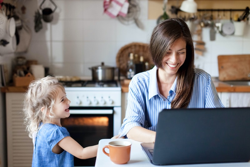 Working mom works from home office on a get paid to site. Happy mother and daughter smiling. Successful woman and cute child using laptop.